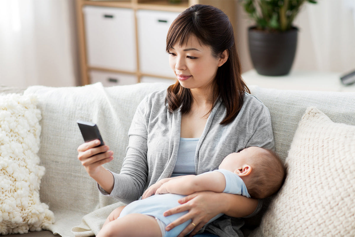mother checking on a phone app while taking care of baby