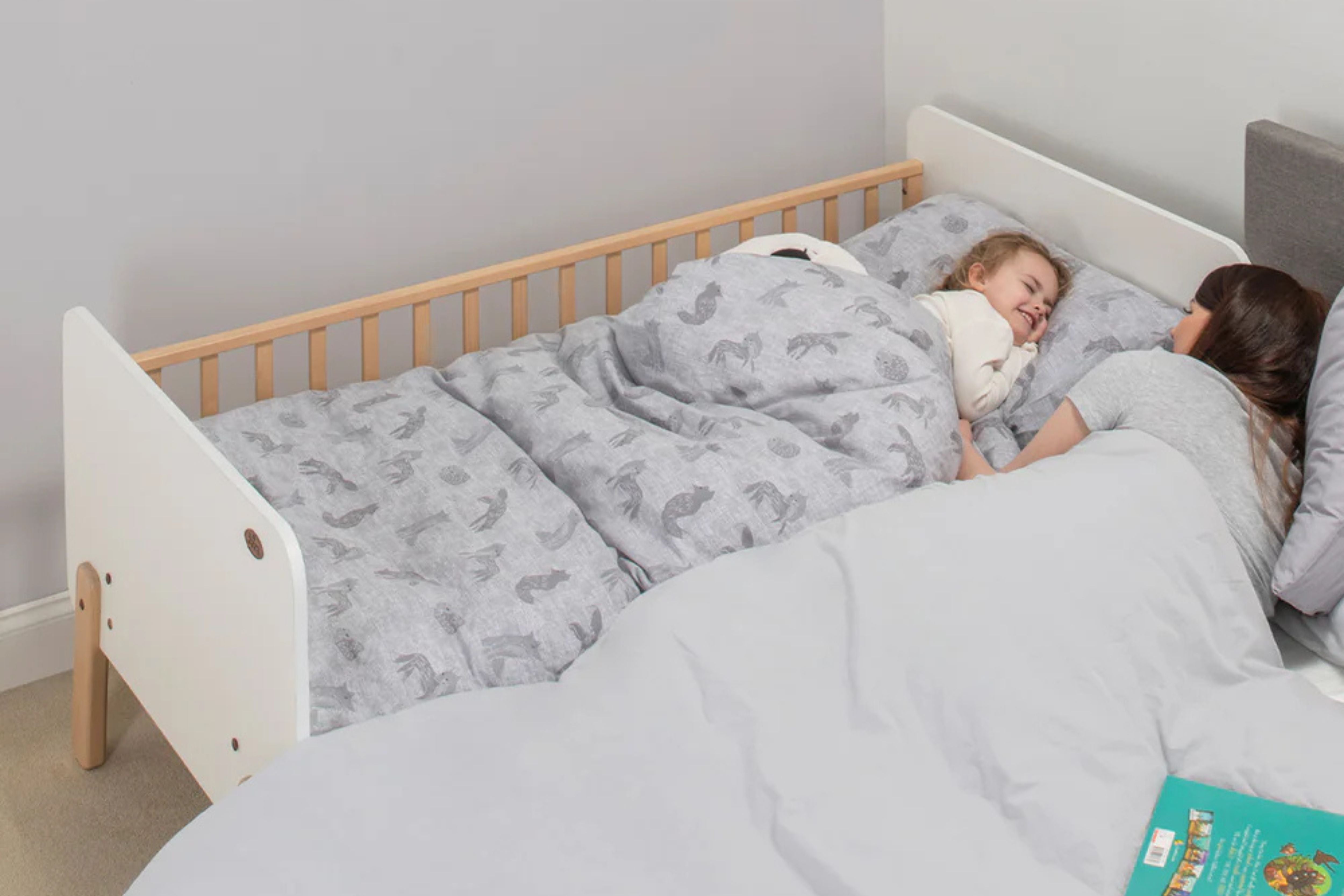 Toddler sleeping in the Boori Natty Bedside Bed placed next to his mother's bed in a cosy bedroom setting