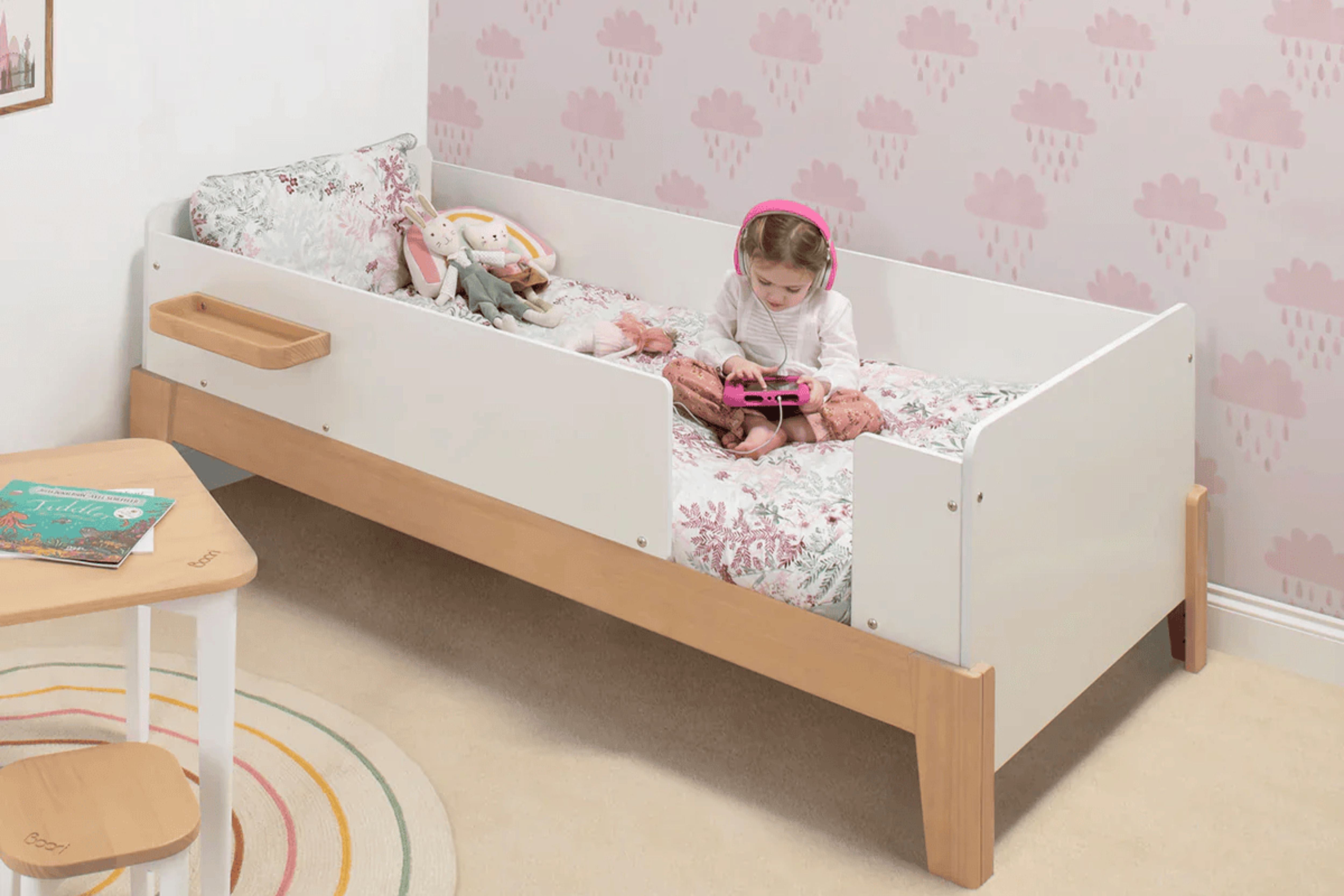 Toddler sitting on the Boori Natty Guarded Single Bed, listening to music and playing games on an iPad in a cosy bedroom setting.