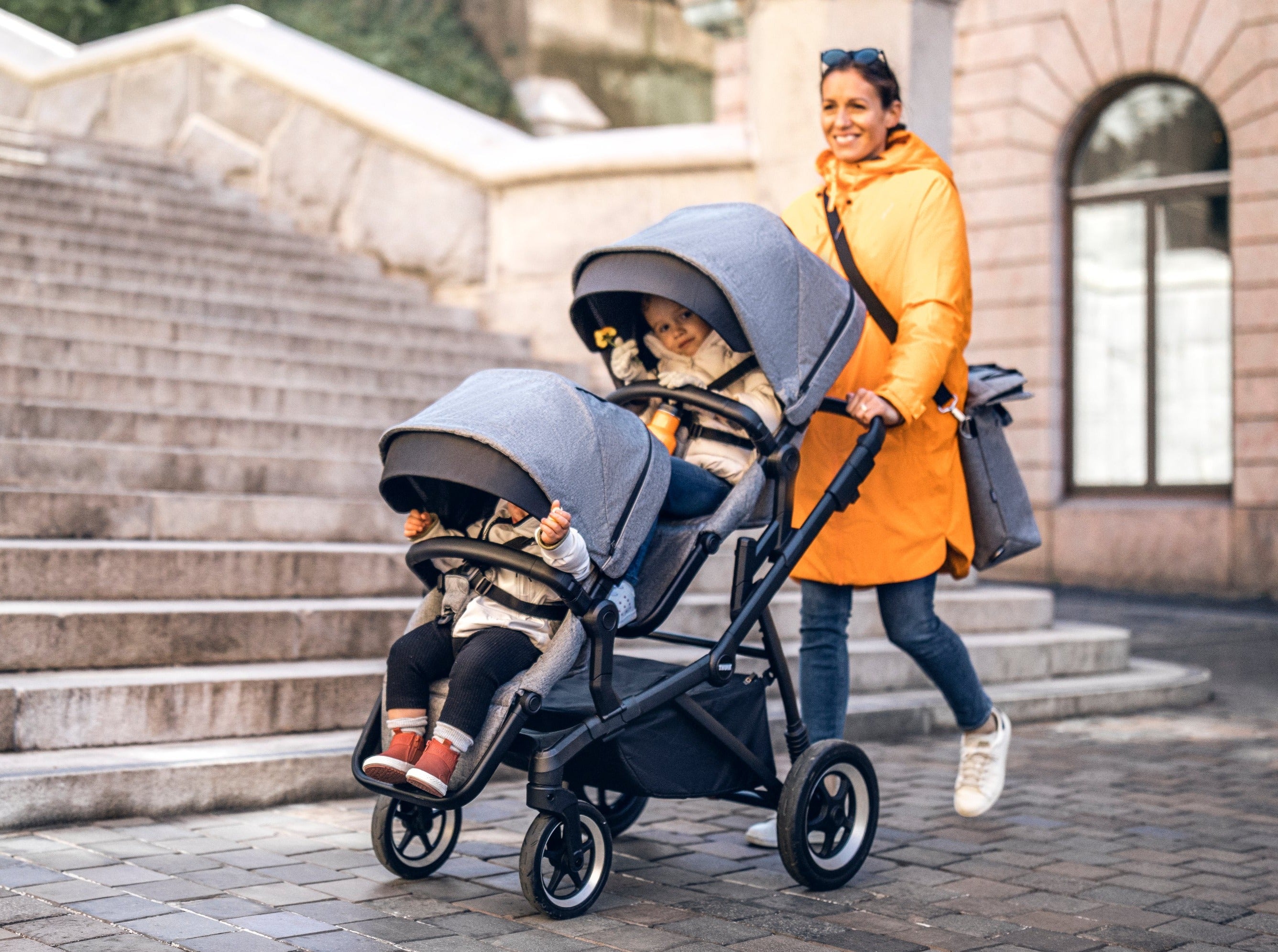 Mum pushing Thule Sleek Double Stroller with sibling seat grey