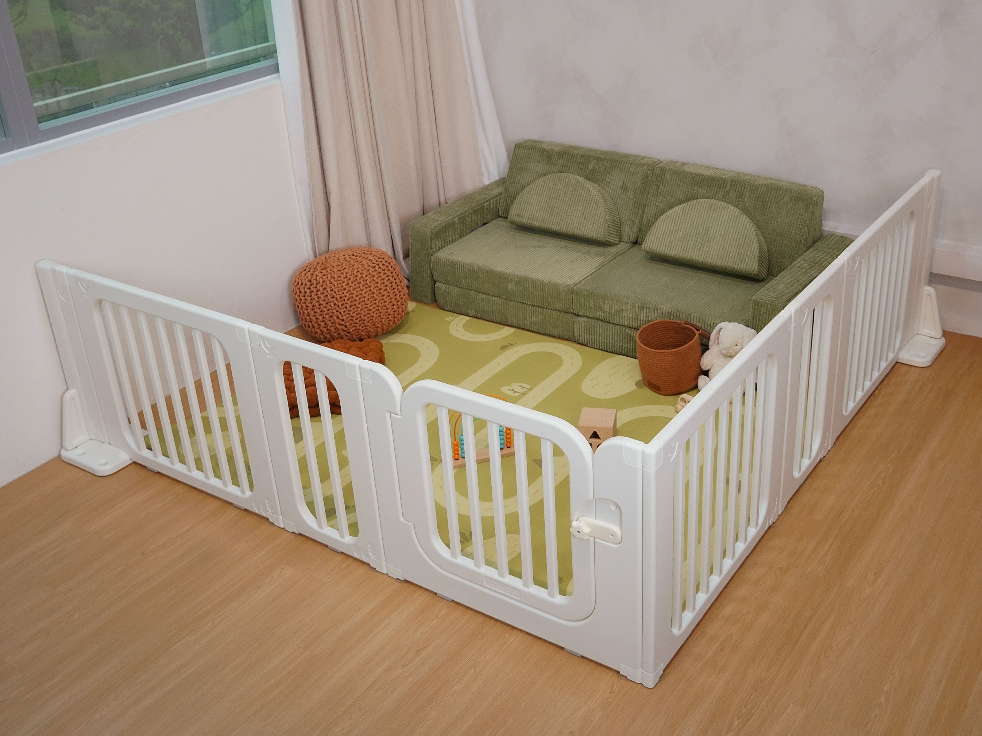 Lollibly Meadow Playpen, supported by the Flexi-Frame Stand, configured neatly against a room corner with the Lollibly Holiday Playmat and Wonderstack Play Sofa in Fern arranged inside