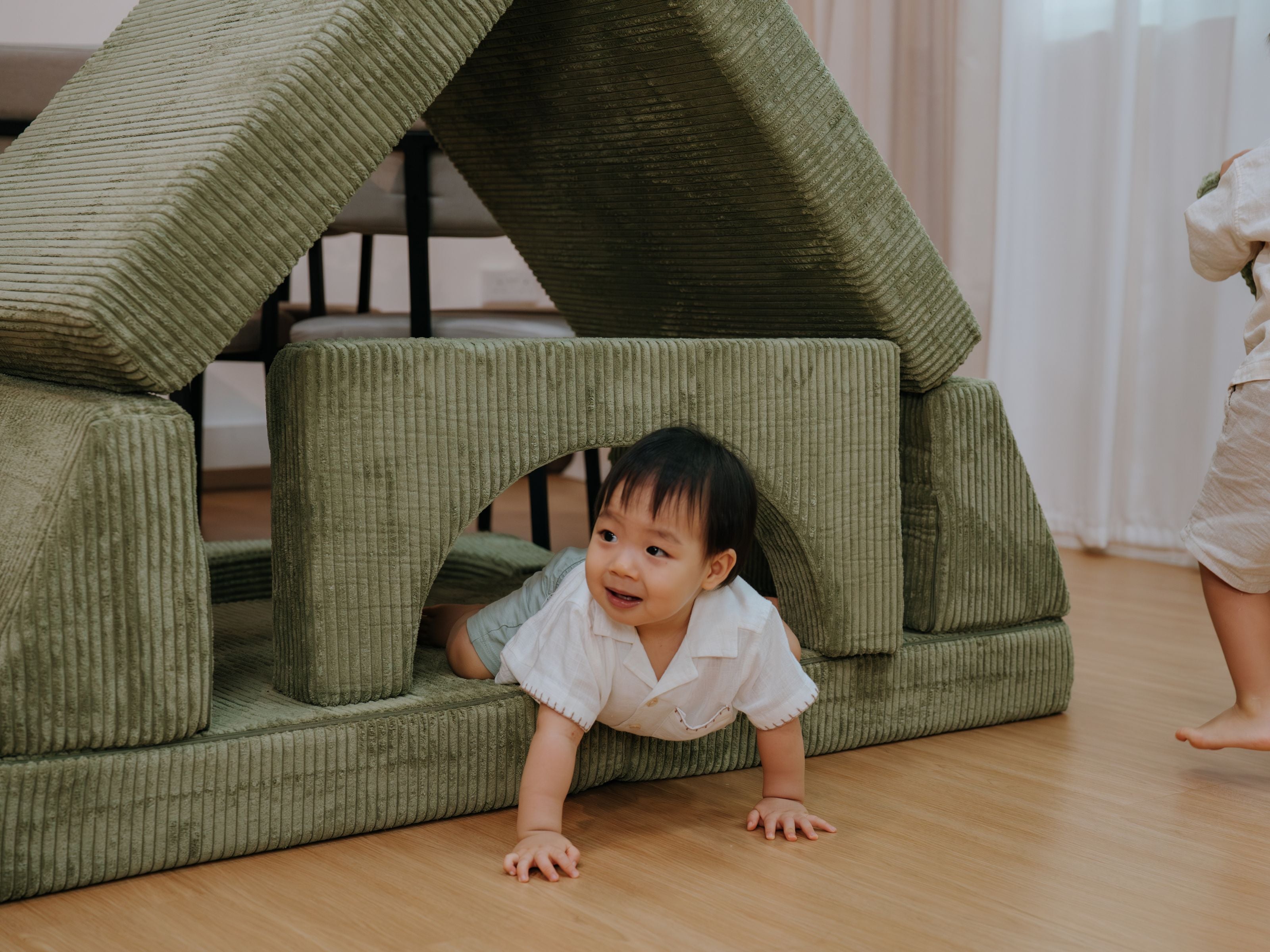 A toddler happily crawling out of a structure built with the Lollibly Wonderstack Play Sofa pieces