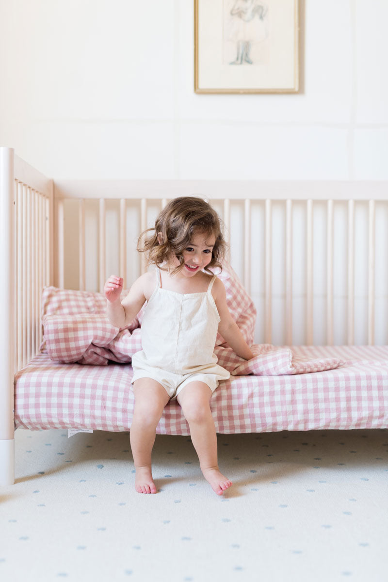 toddler girl sitting on crib mattress lined with pehr checkmate blossom sheet