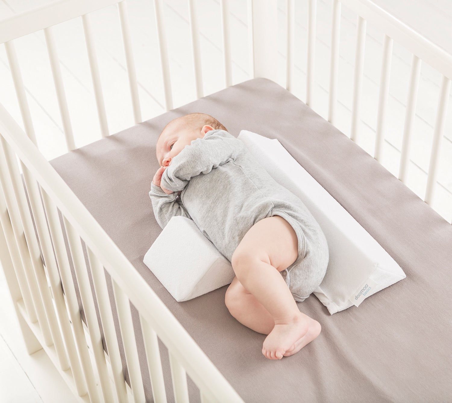 baby lying in crib on doomoo baby sleep side positioner