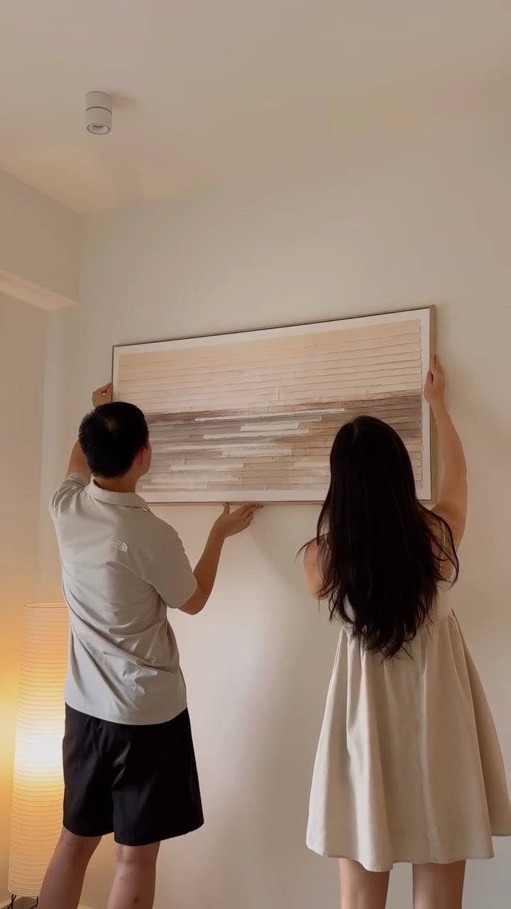 Lady hanging up a piece of wall art on a blank wall