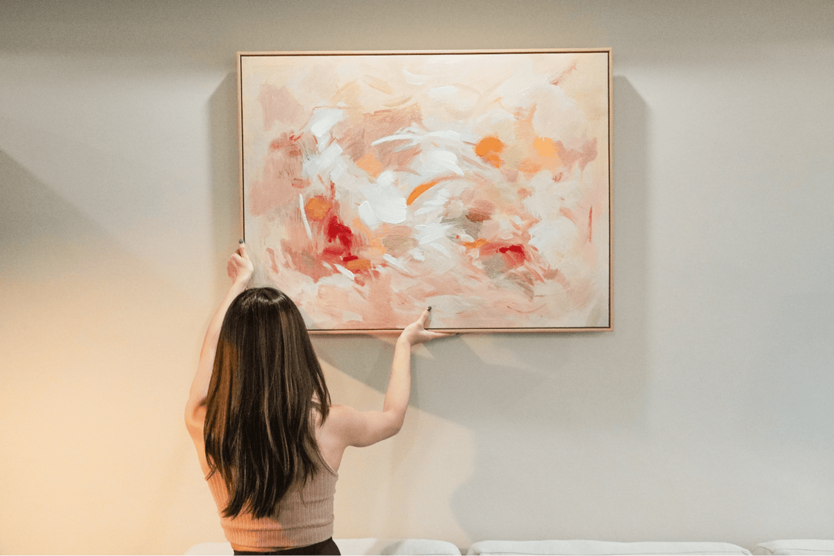 Lady hanging up a piece of wall art on a blank wall