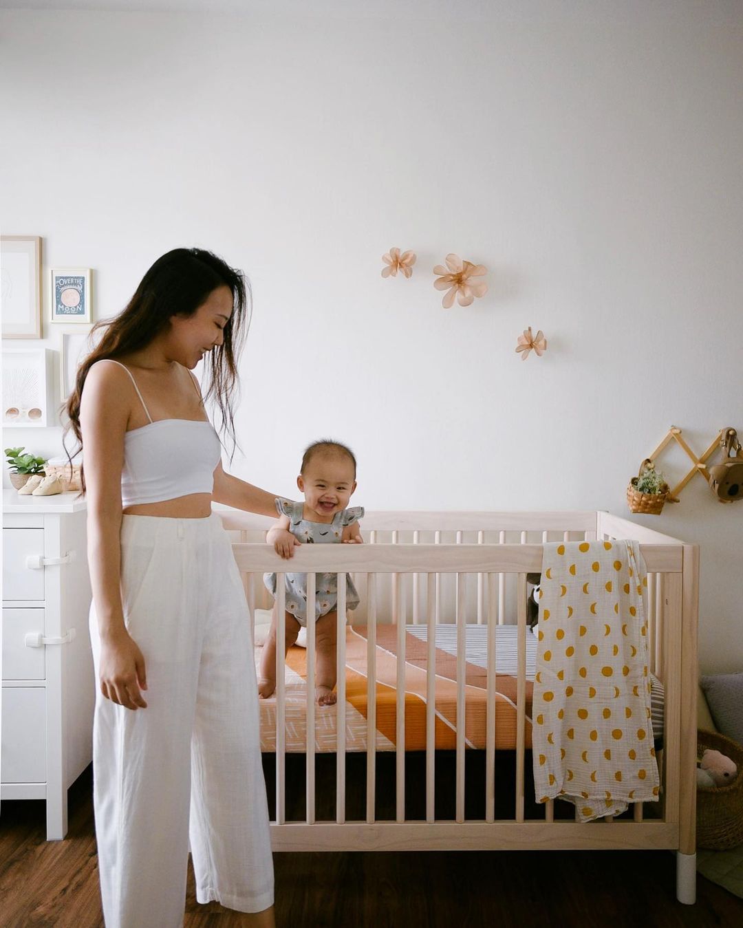 baby standing in crib while mum holds her