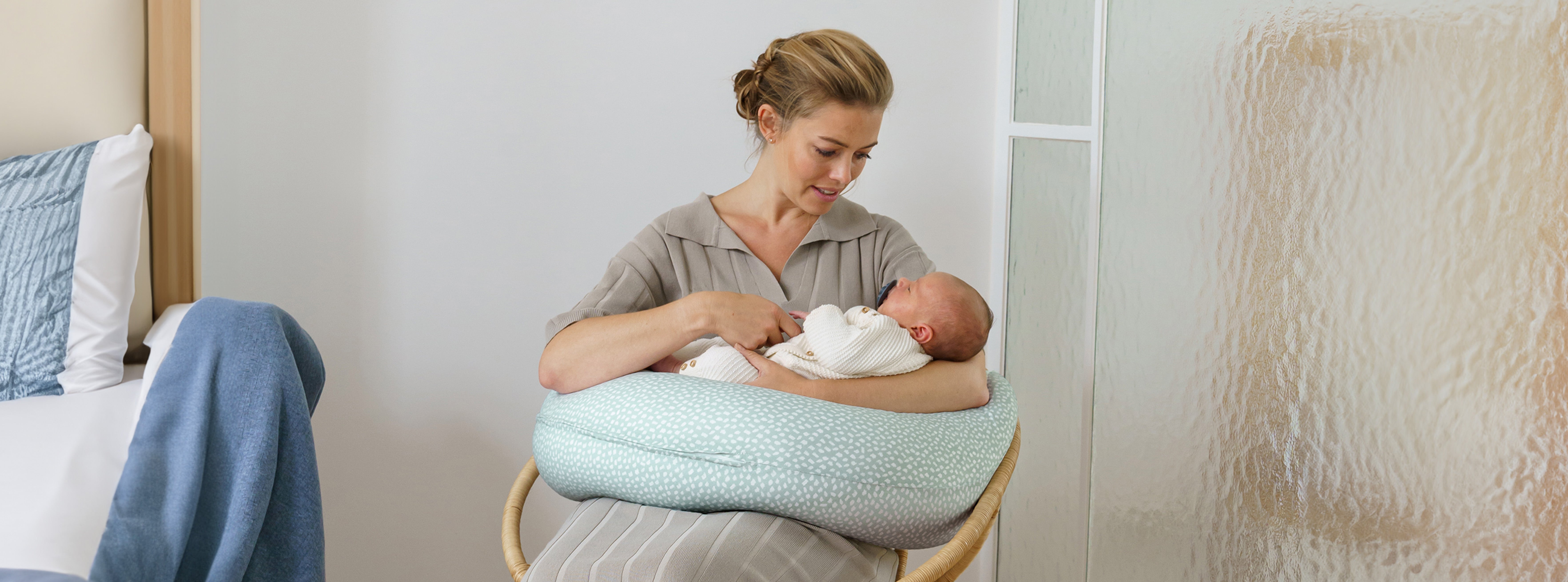 mum smiling at newborn baby nursing on pregnancy nursing pillow in bedroom