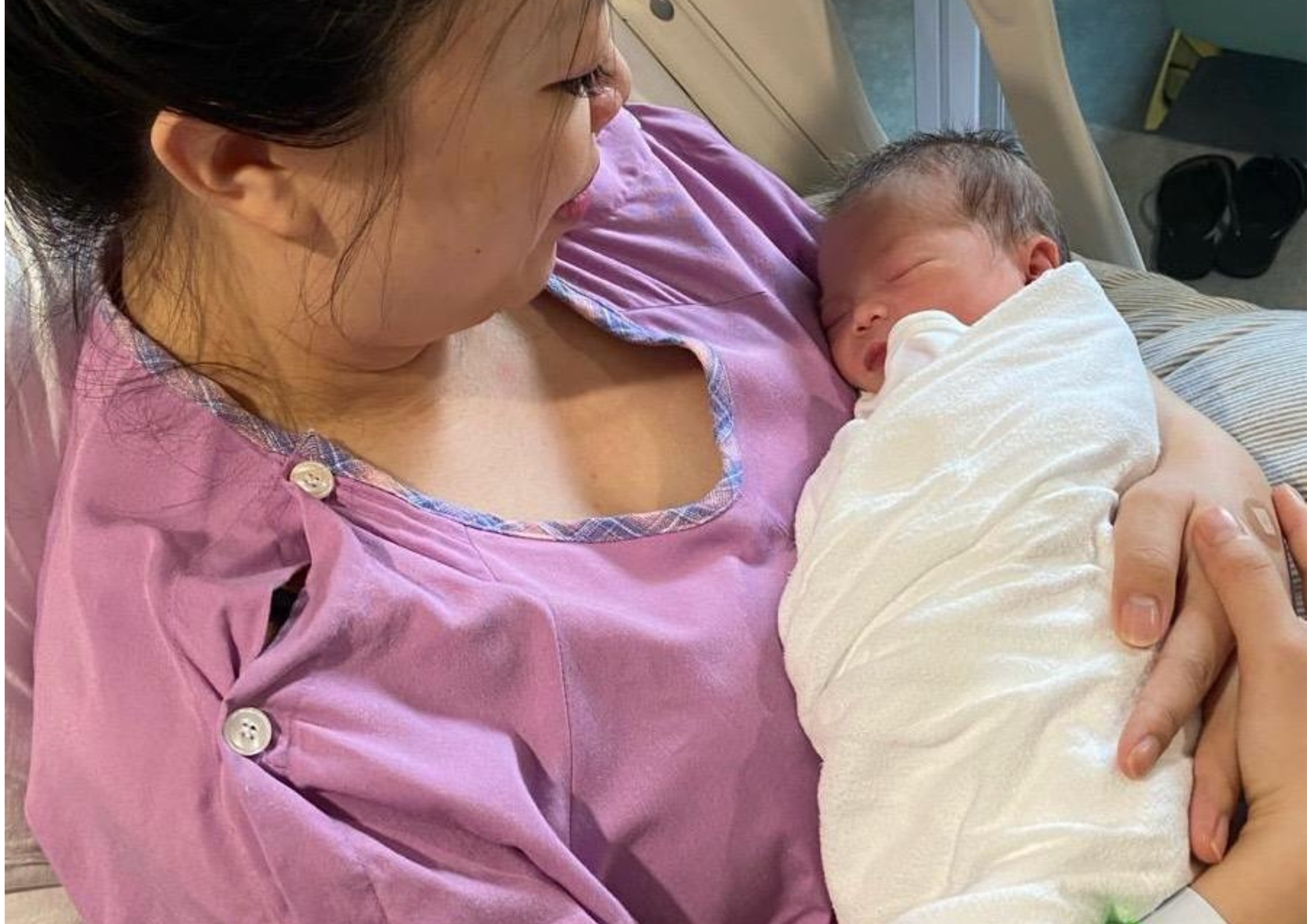 Woman holding a newborn baby wrapped in a white swaddle.