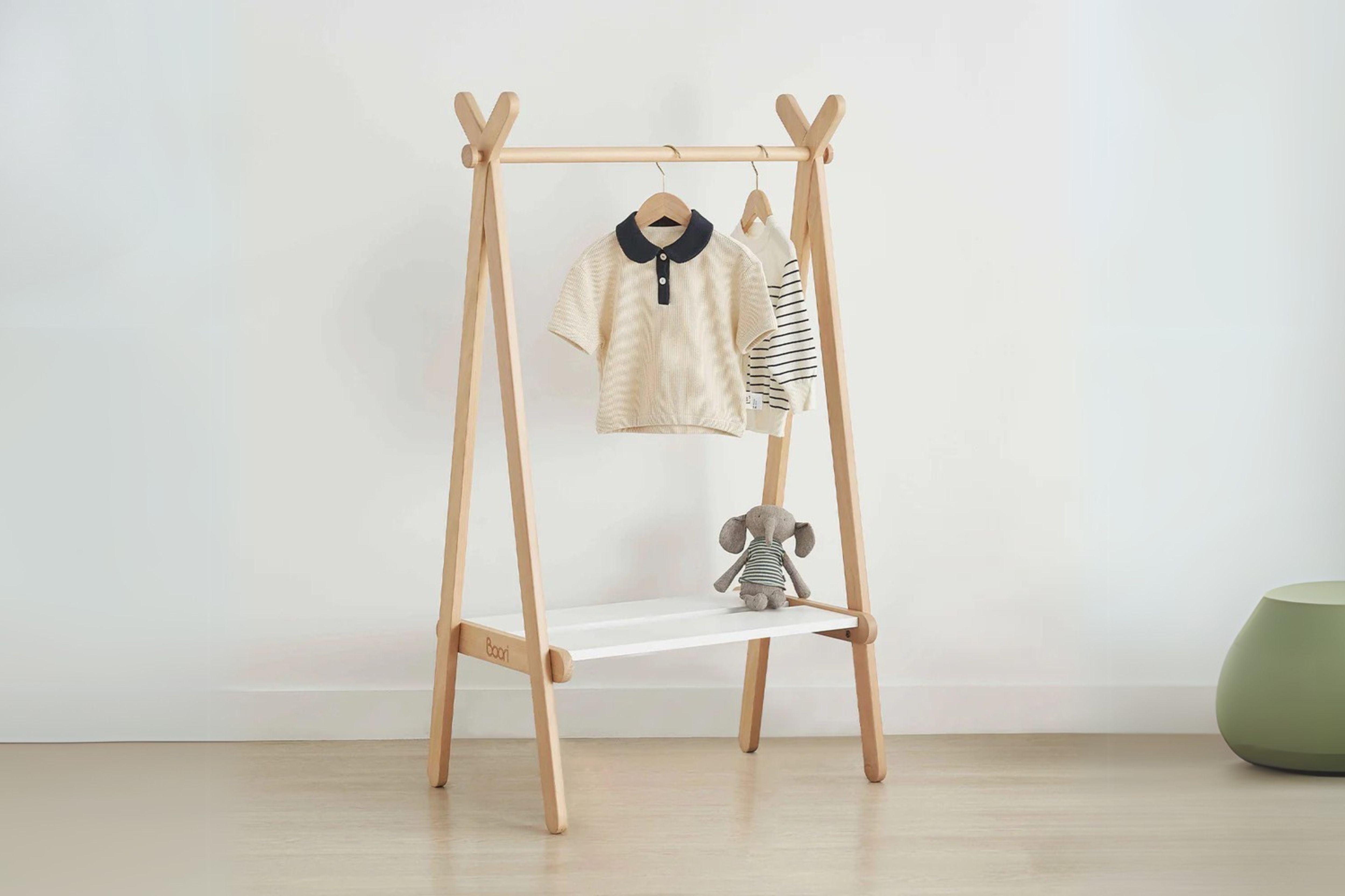 Boori Forest Clothing Rack placed in the center of a nursery, holding a few neatly hung baby clothes and displaying some toys on the lower shelf