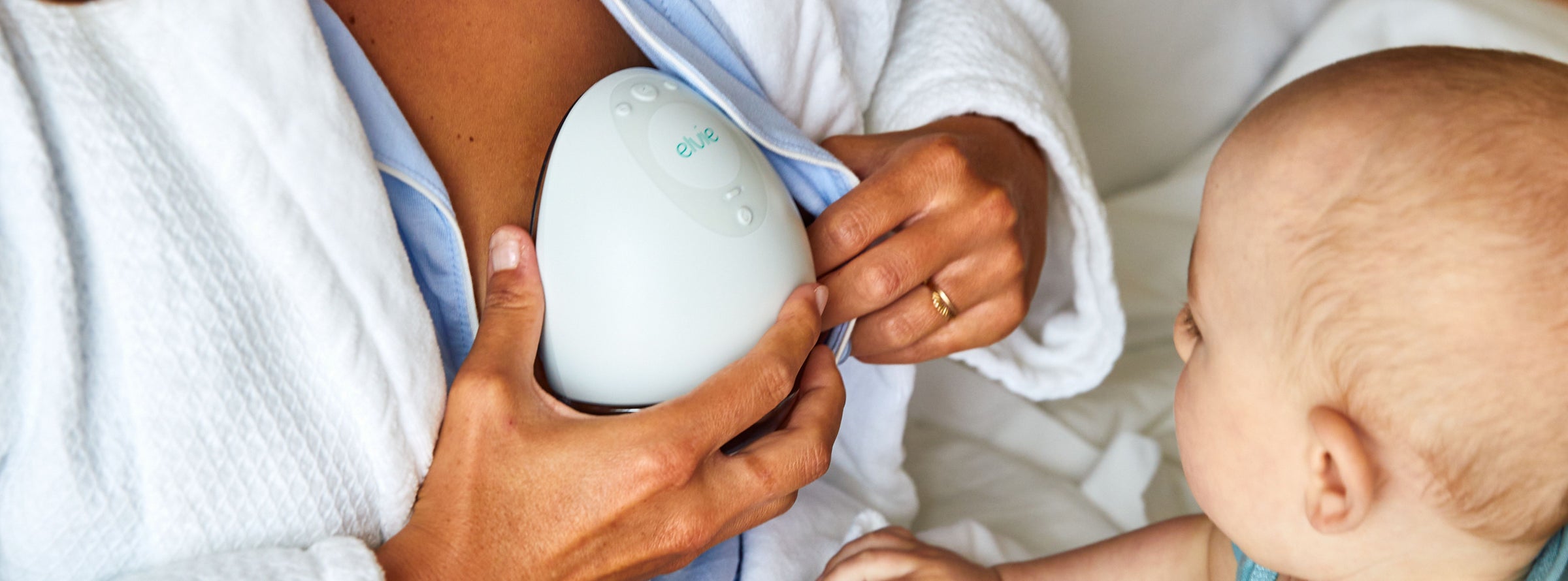 mother using a wearable breast pump with newborn beside her
