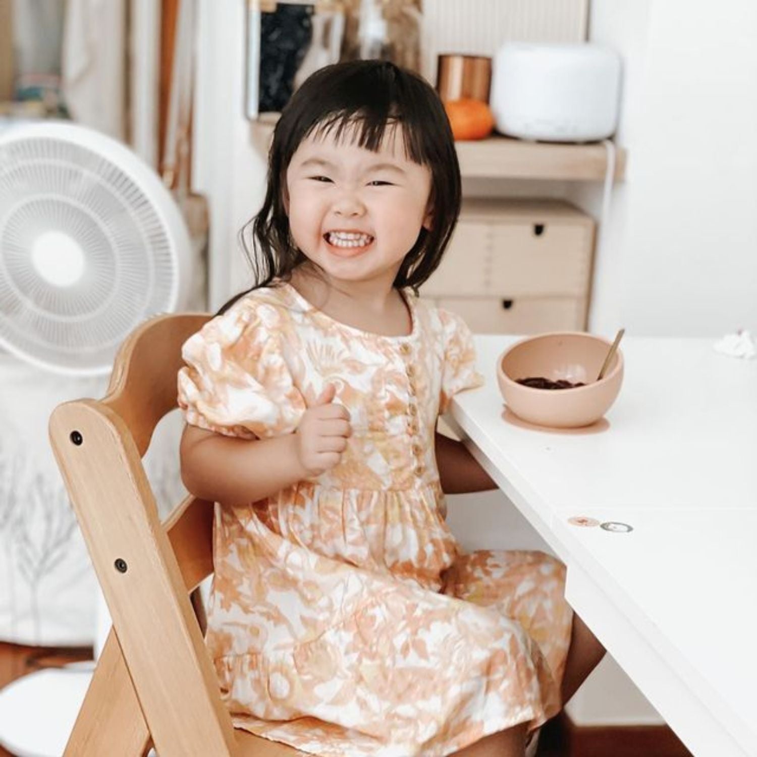 Child sitting at a table on a wooden high chair, smiling.