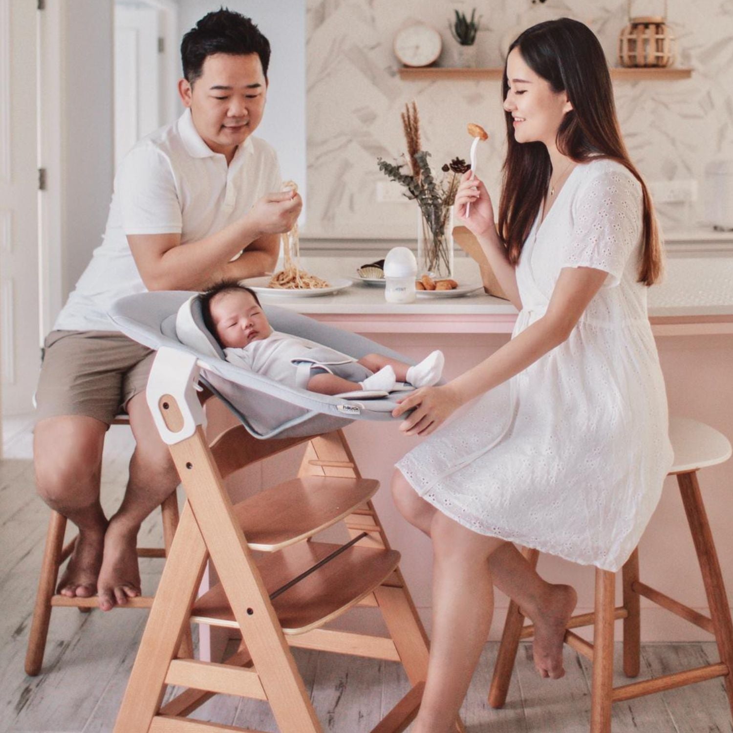 Family of three in a modern kitchen with a baby in a wooden high chair.