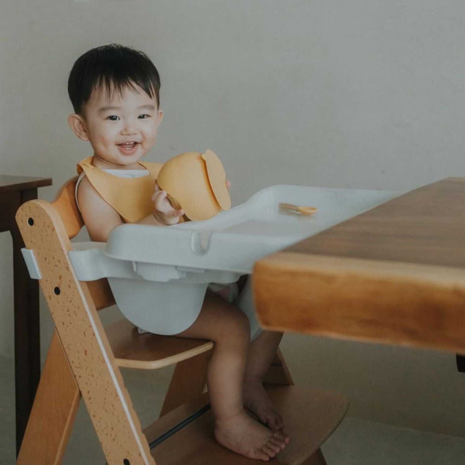 Child sitting in a wooden high chair with a wooden table in the background
