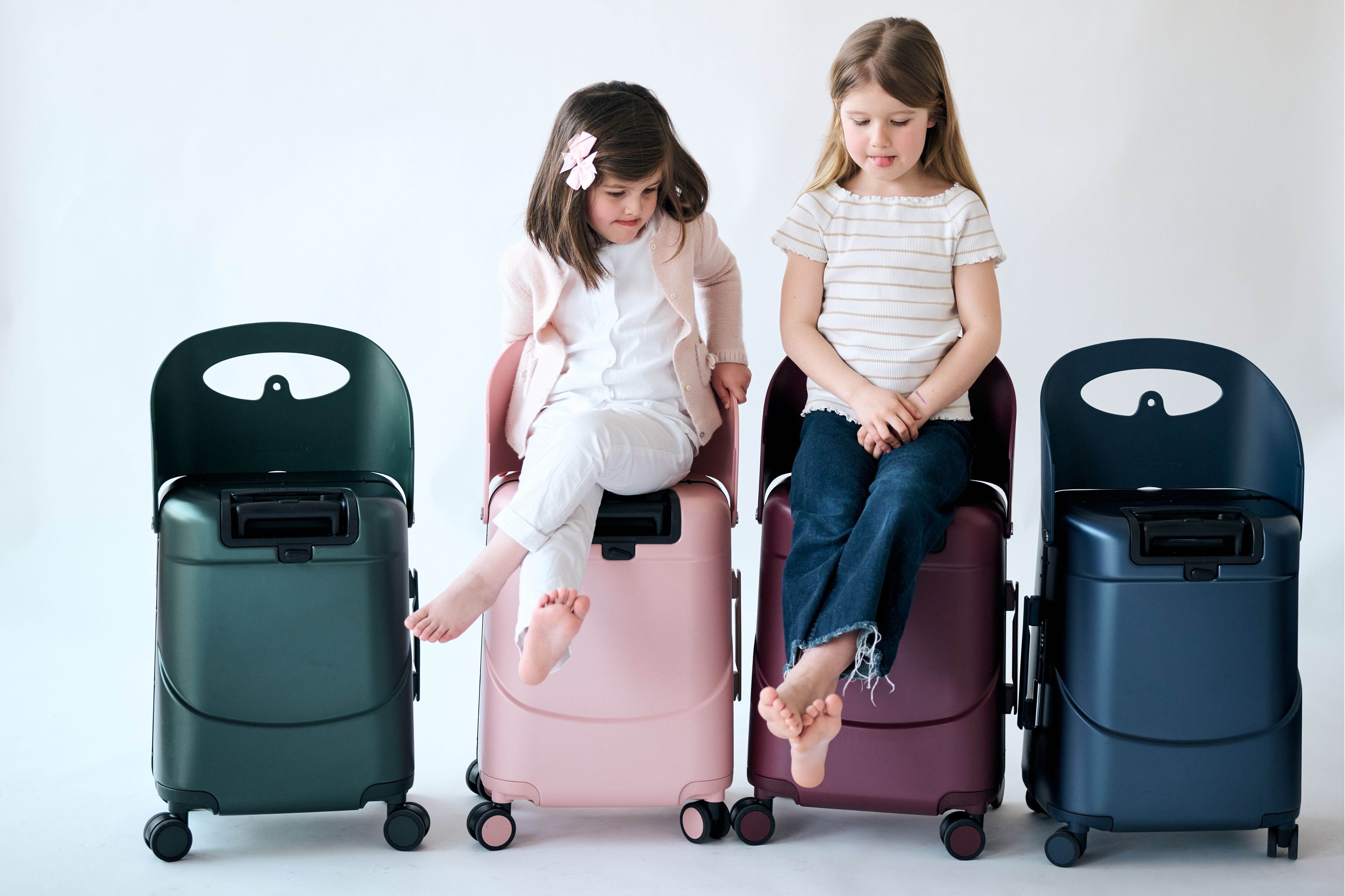 Two children seated comfortably on the built-in ride-on seats of the MiaMily Carry On Plus 18” Luggage
