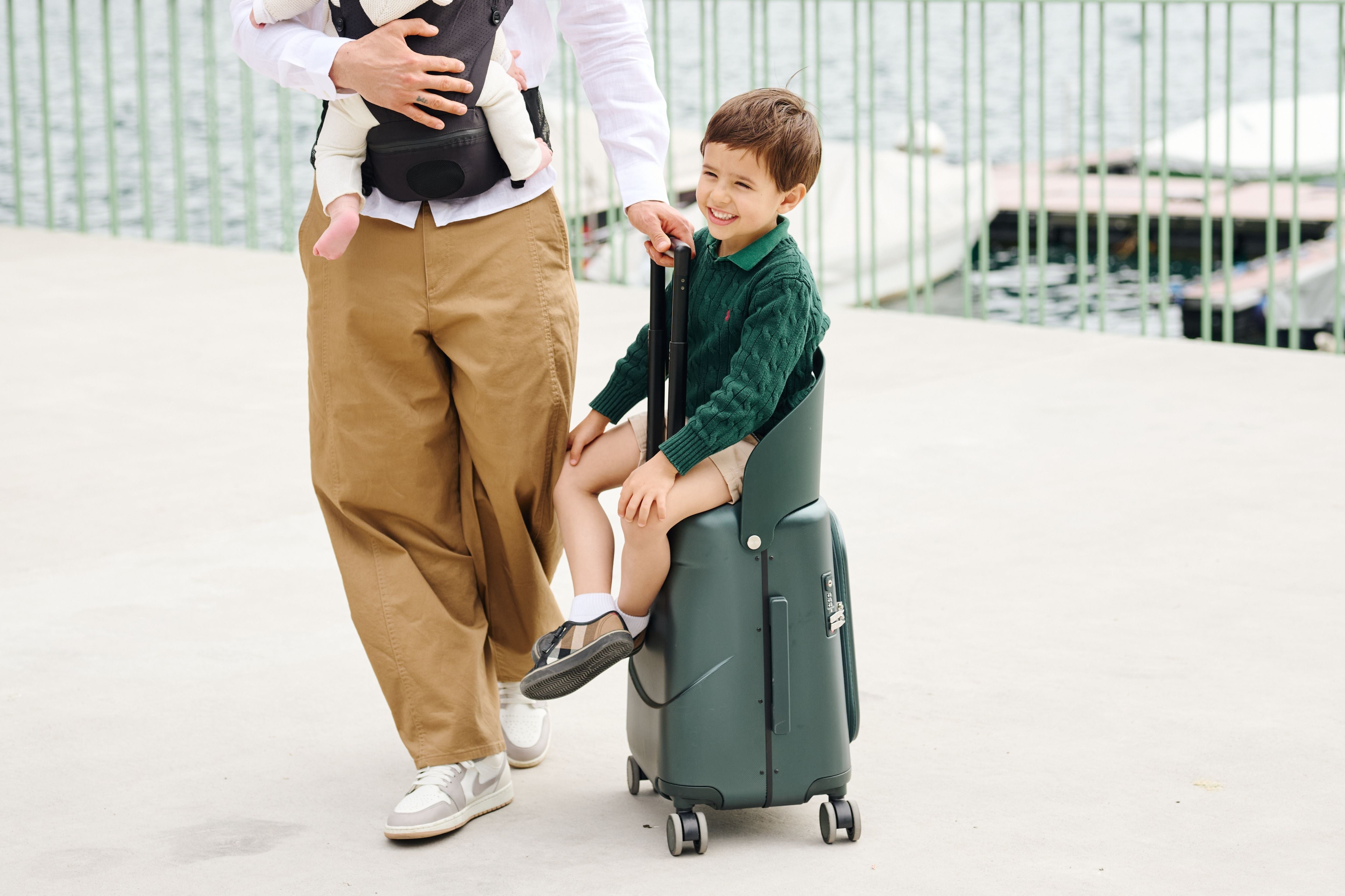 A child seated on the built-in ride-on seat of the MiaMily Carry On Plus 18” Luggage while being pushed along