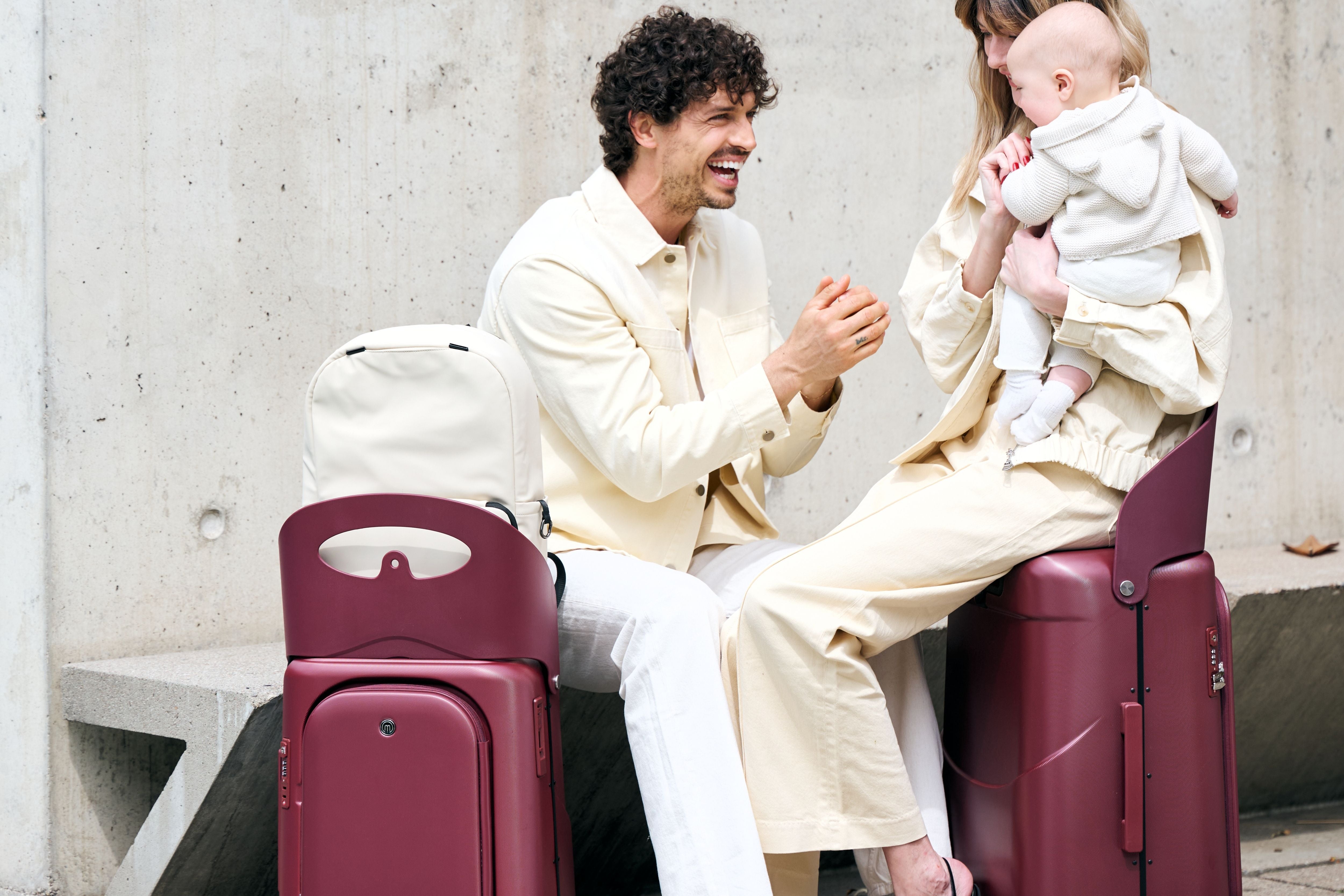 A woman with a baby sitting comfortably and securely on top of the MiaMily Carry On Plus 18” Luggage