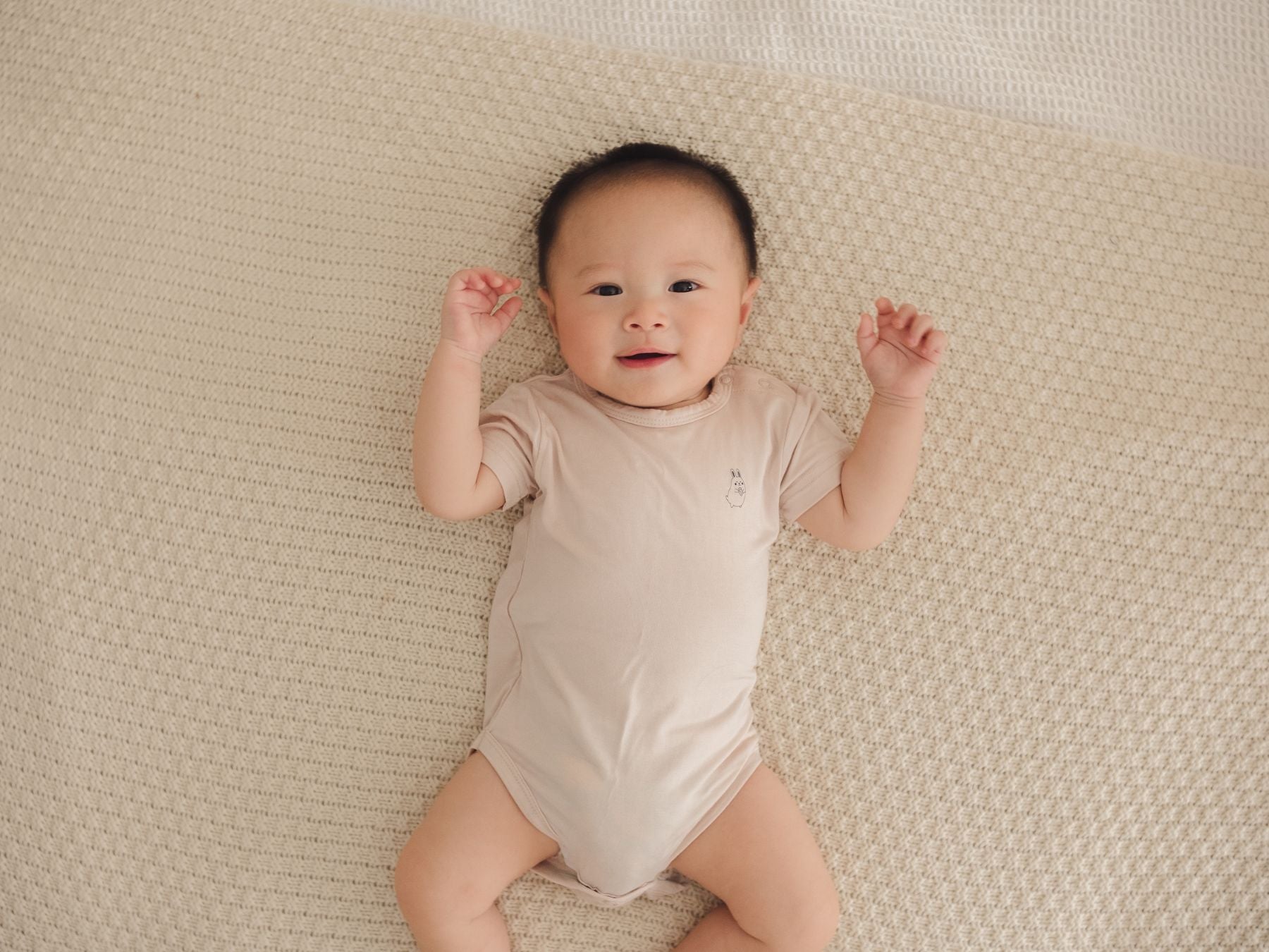 Baby lying comfortably on a bed, wearing a beige onesie