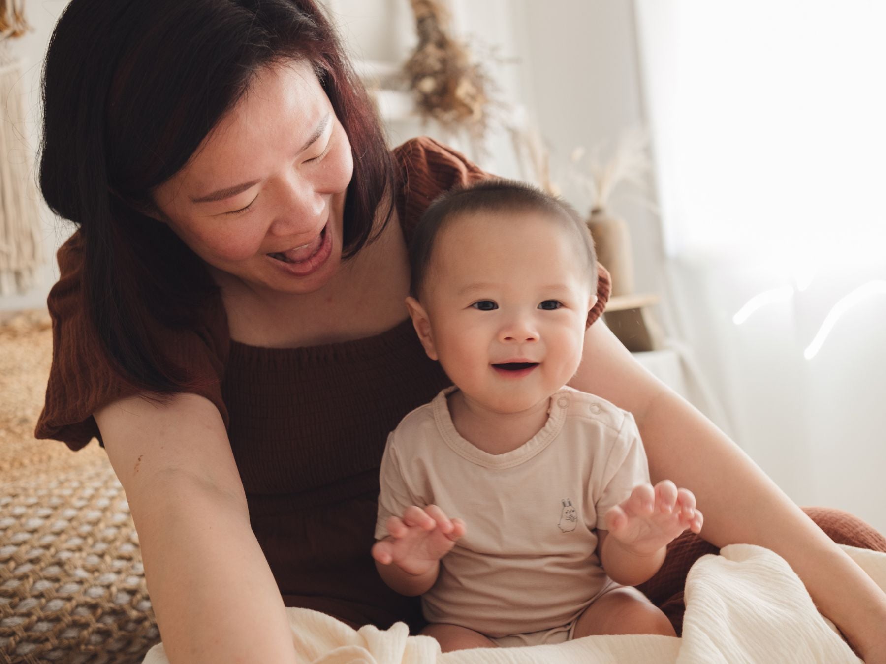 Woman cradling a baby on her lap while the baby wears a beige onesie