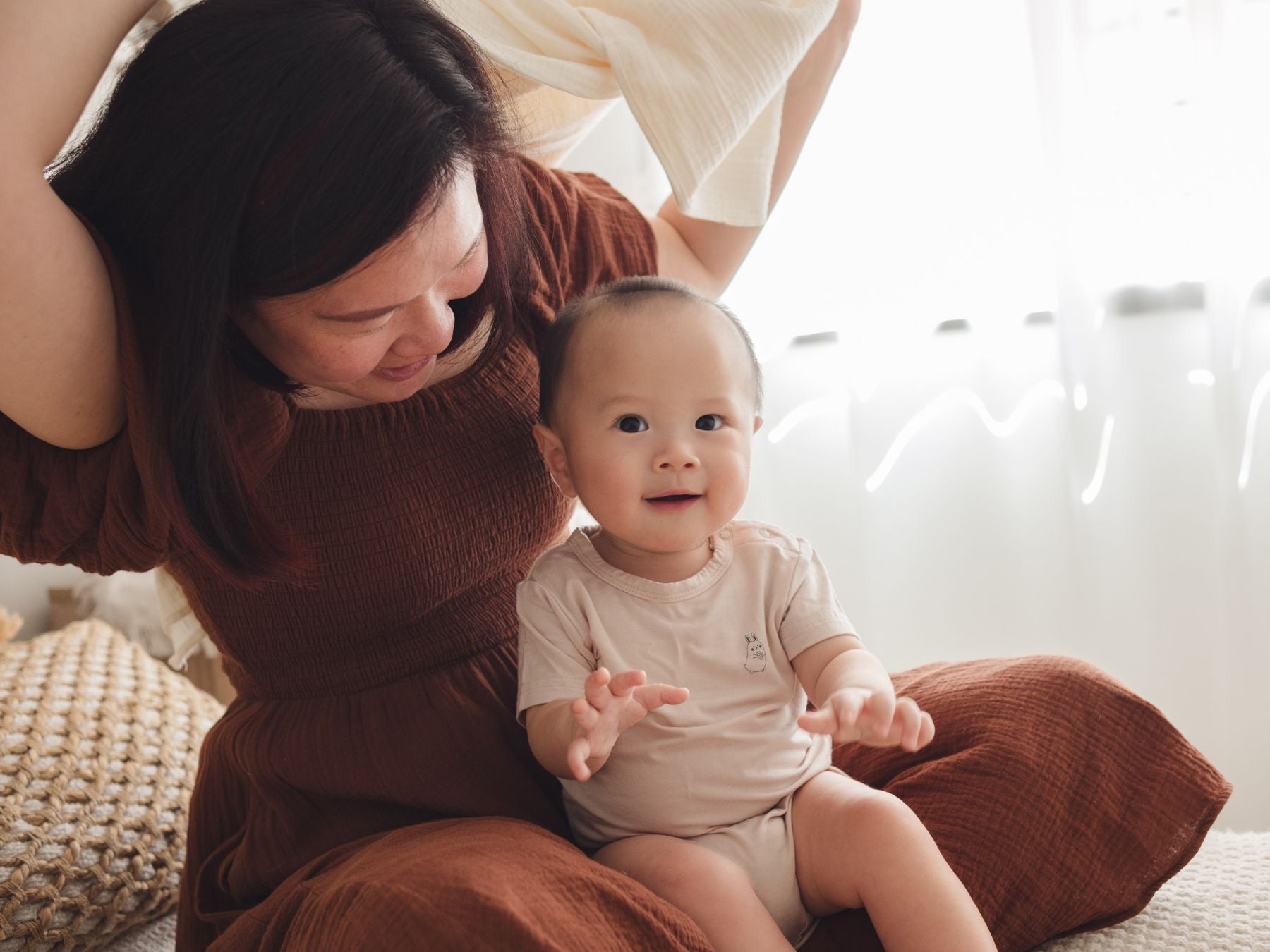 Smiling baby in a beige onesie sitting on mum’s lap
