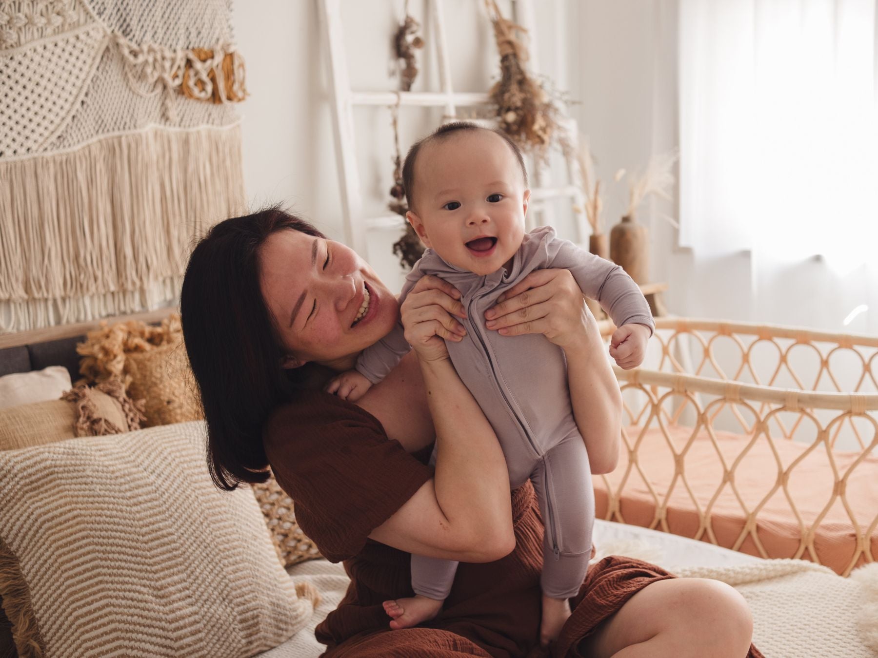 Woman holding up a baby wearing a lavender sleep suit