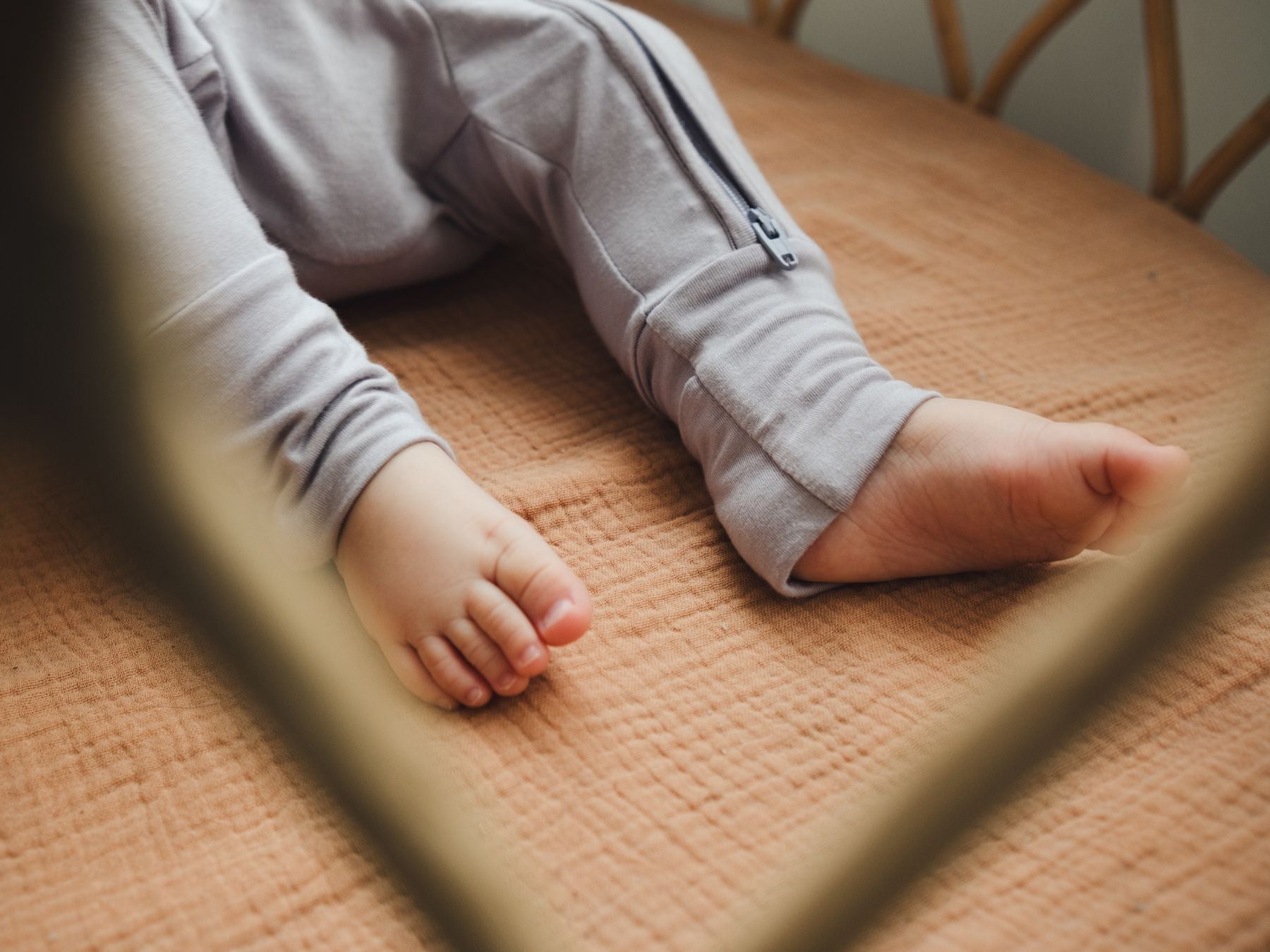 Baby lying in a crib wearing a lavender sleepsuit, showing the fold-over foot mitten detail