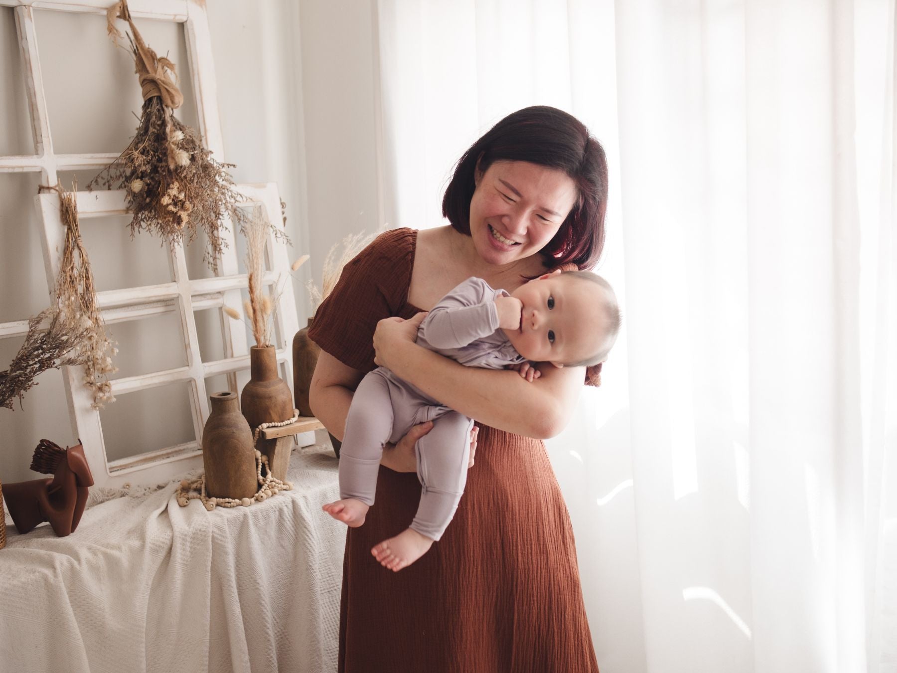 Woman holding her baby close as they tilt to one side, with the baby wearing a lavender sleep suit