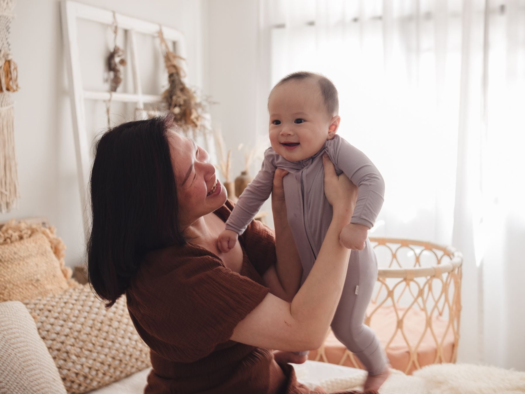 Smiling woman cuddling a baby in a cosy bedroom, with the baby dressed in a lavender sleepsuit
