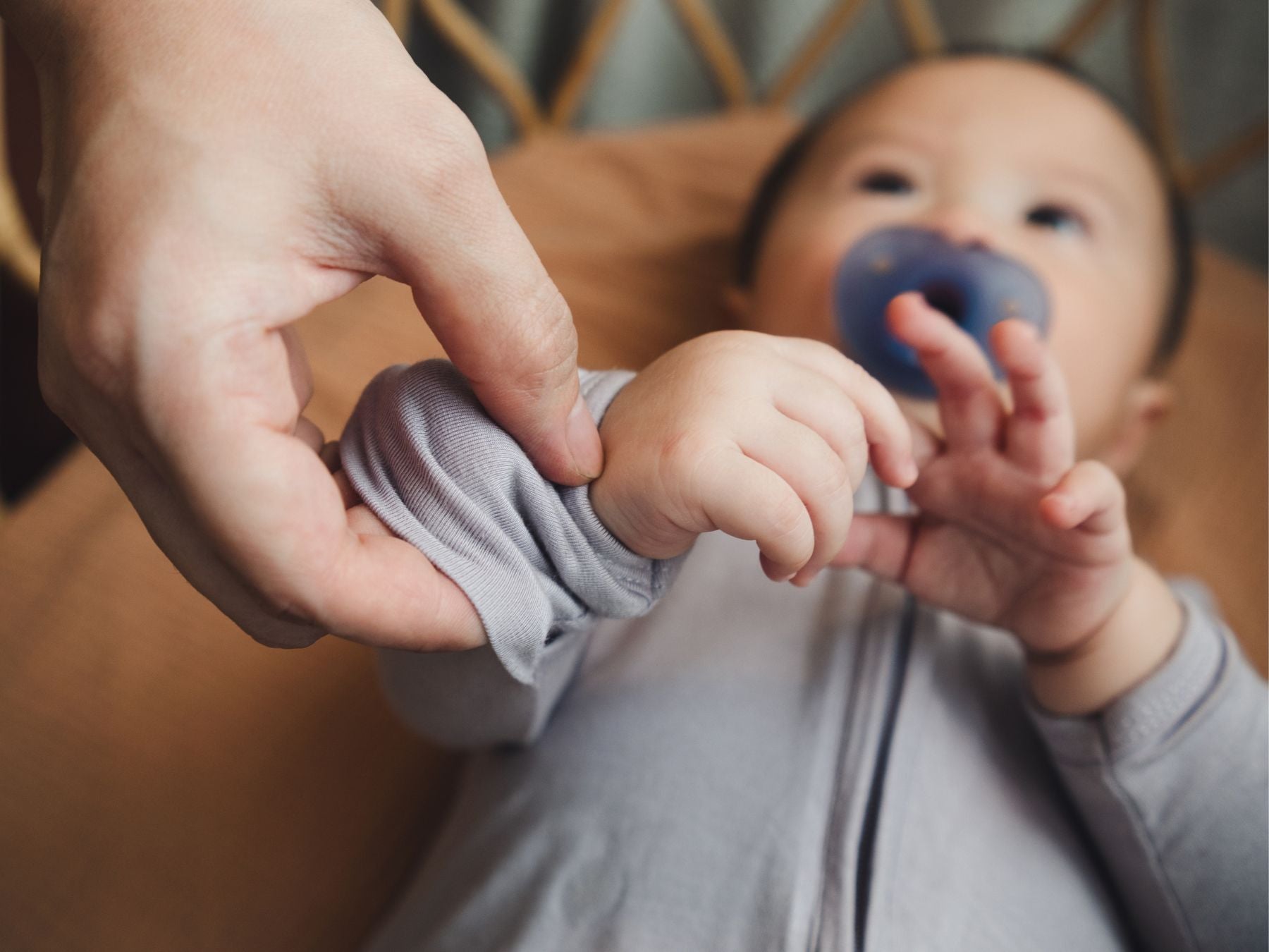Baby lying in a cot while an adult flips over the sleep suit hand mitten