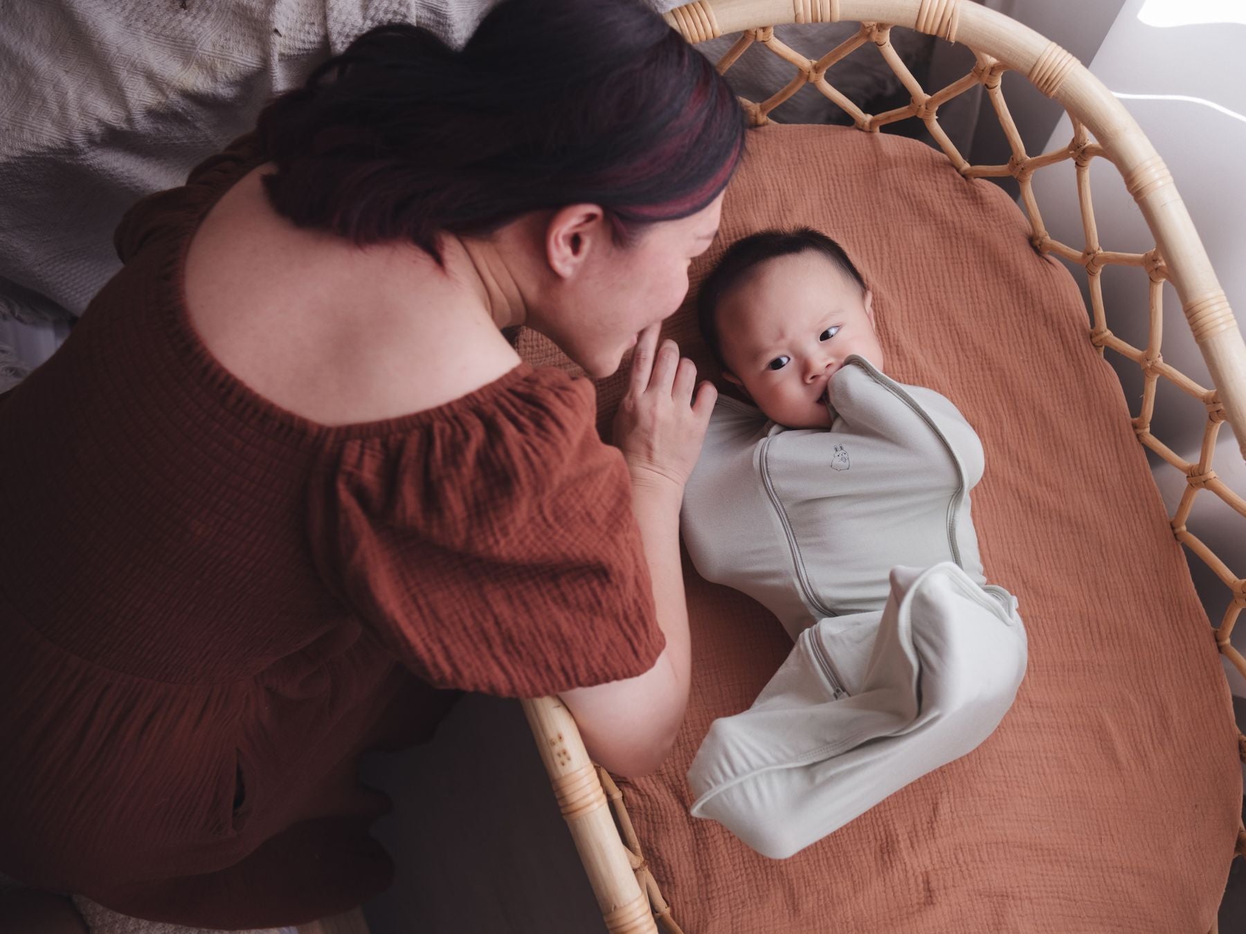 Mother leaning over the cot, looking lovingly at her baby wrapped in a swaddle bag