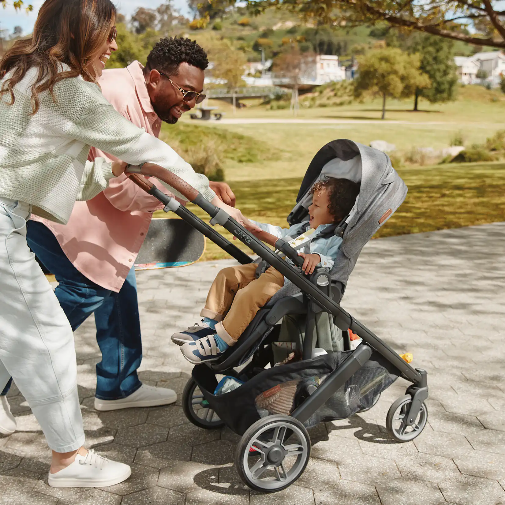 Family with a child in the UPPAbaby Cruz V3 Stroller walking outdoors on a path #color_greyson