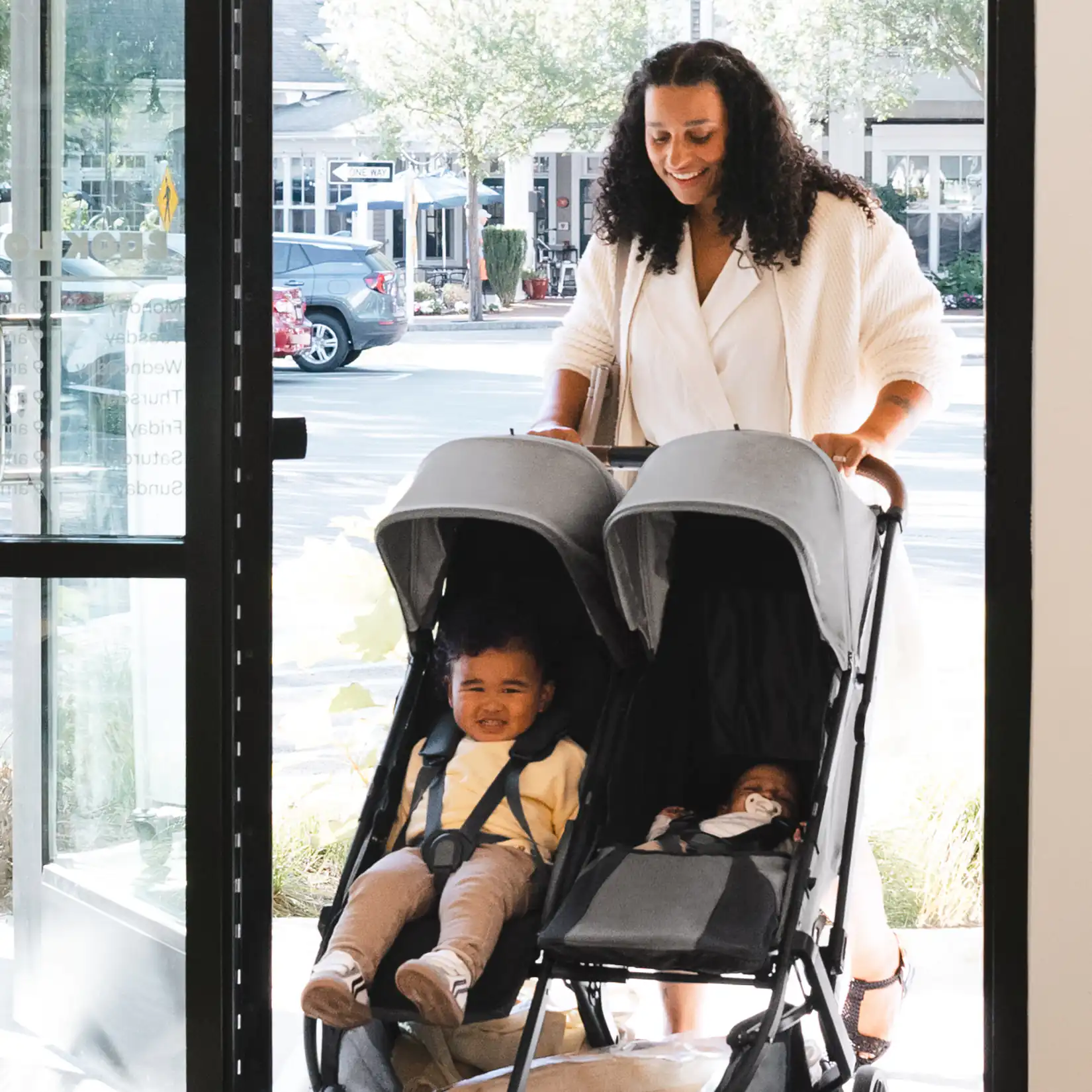 Woman pushing the UPPAbaby Minu Duo double stroller with two children #color_greyson