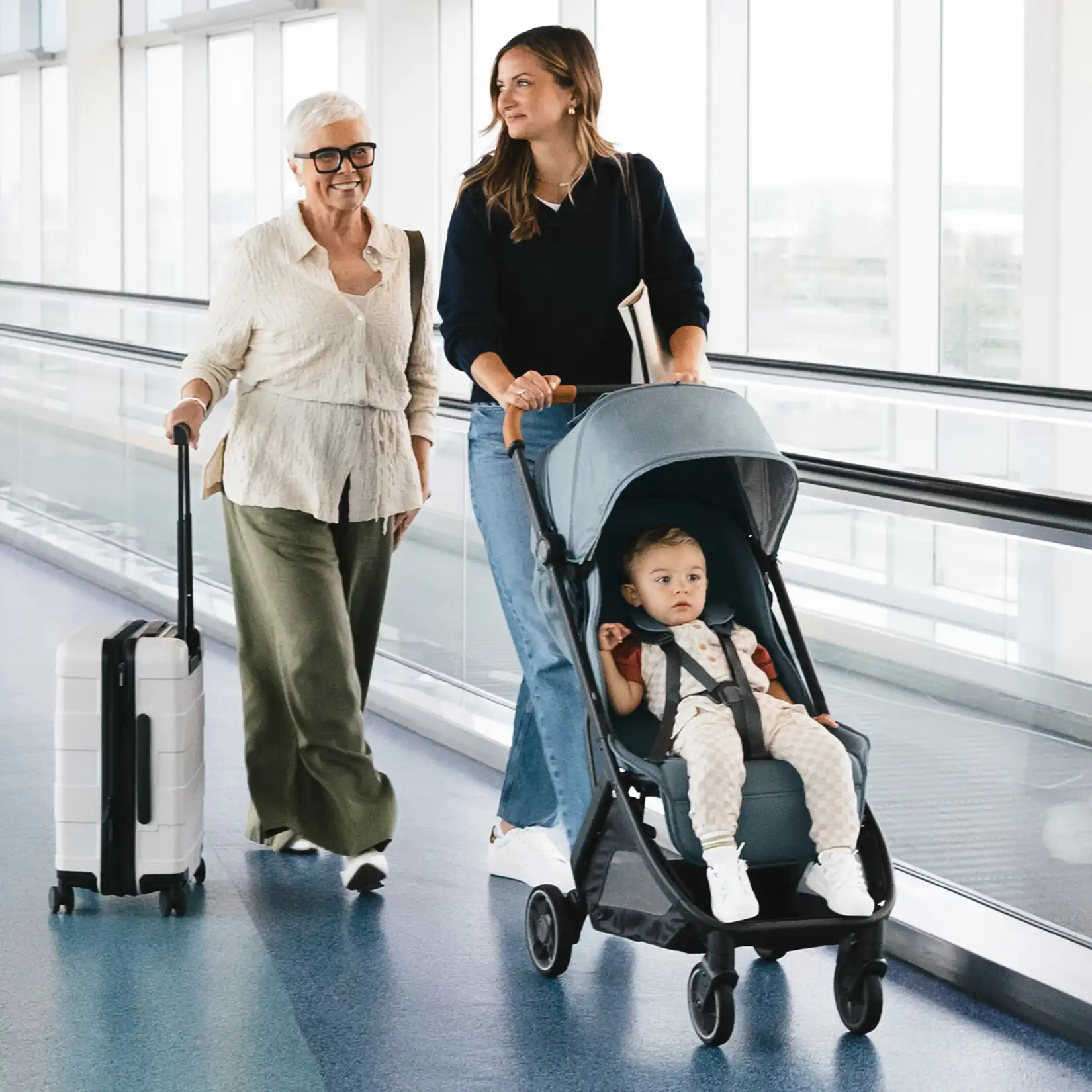 Woman pushing the UPPAbaby Minu stroller with a child inside, walking through an airport with another woman carrying a suitcase #color_dillan