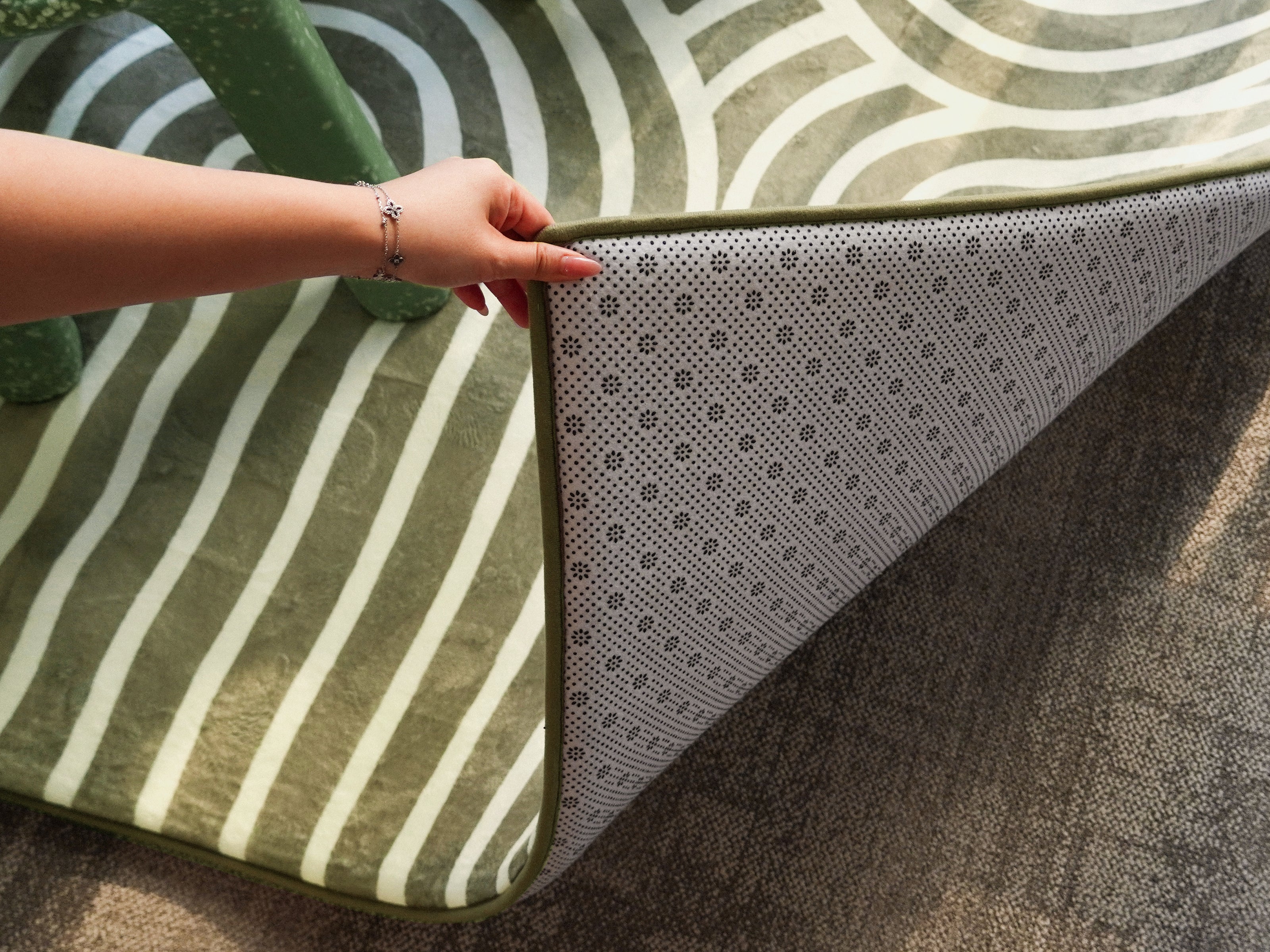 A close-up of the Lollibly Kaya Plush Playmat being pulled back to show its textured non-slip backing.