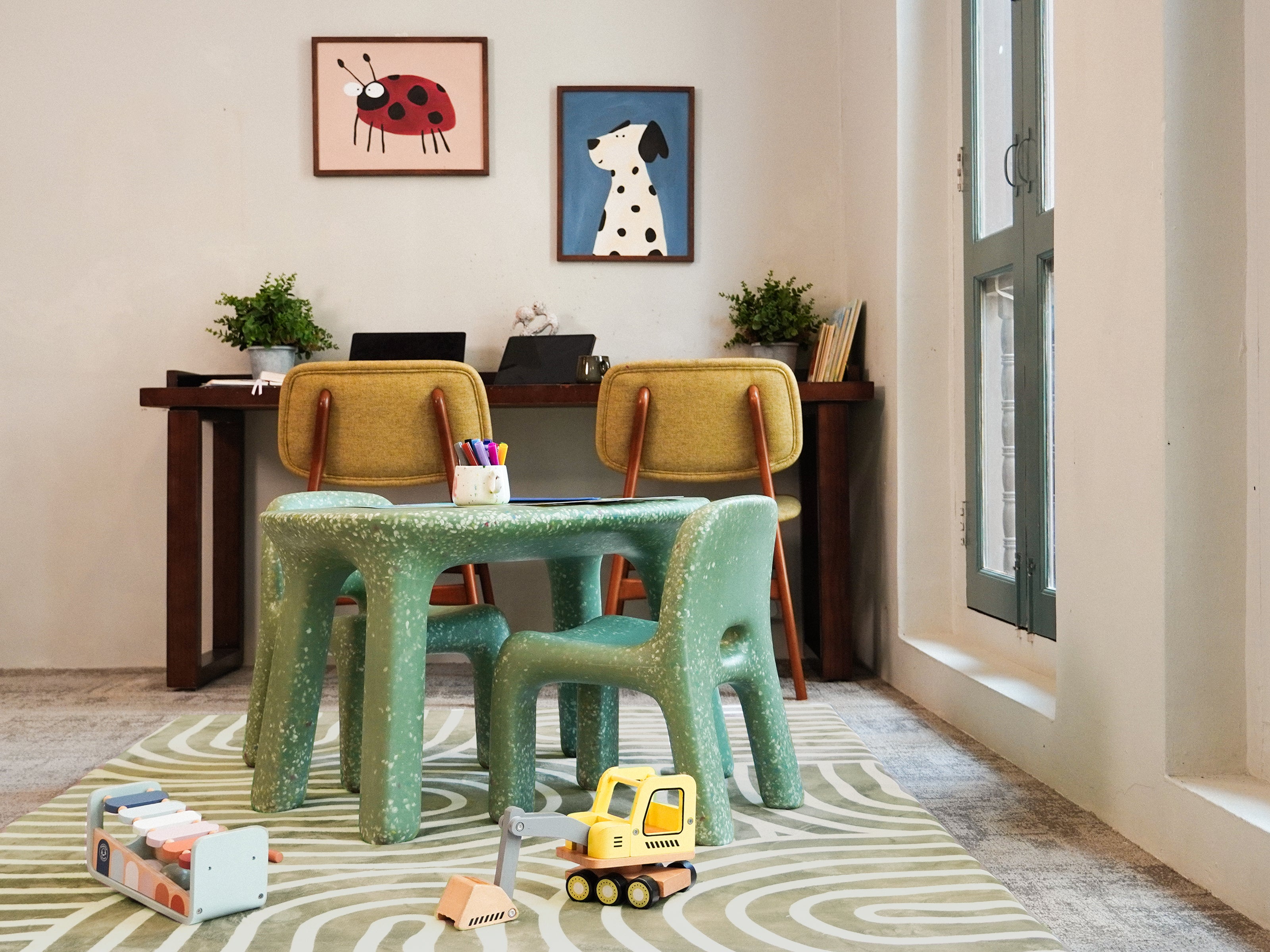A cosy study corner featuring a green speckled table and matching chairs placed on the patterned Lollibly Kaya Plush Playmat.