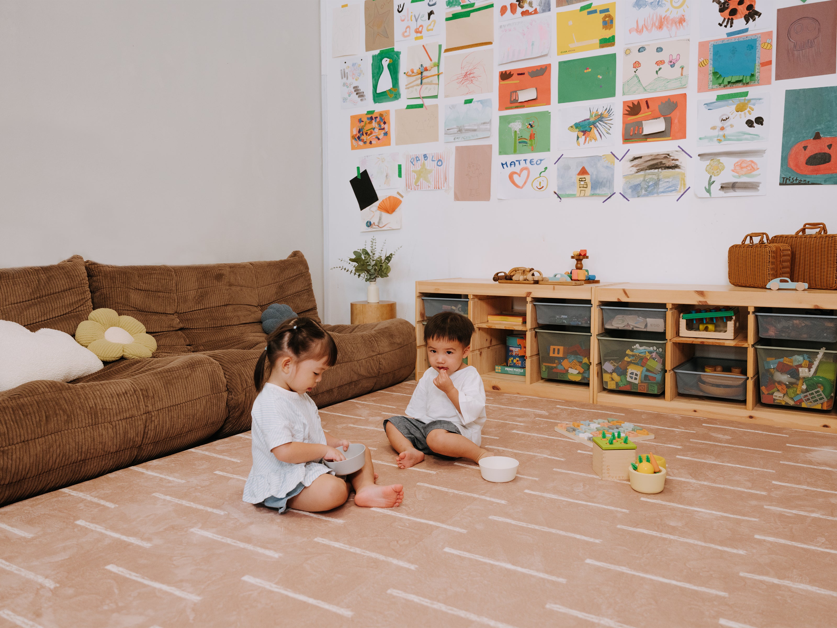Two young children sitting and playing together on the Lollibly Shortbread Plush Playmat in a cosy living room.