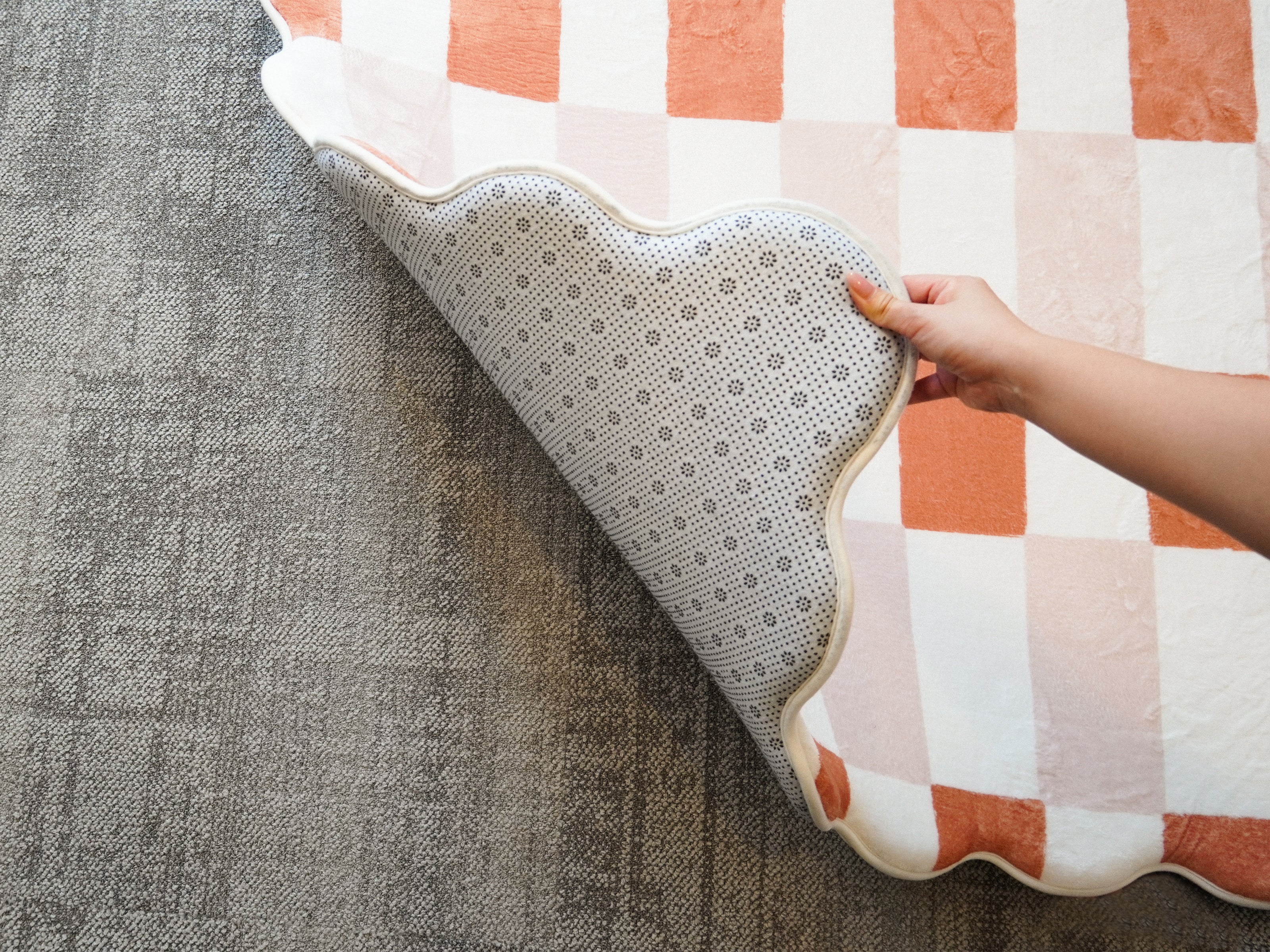A hand lifting the corner of the Lollibly Waffle Plush Playmat to reveal its non-slip underside.
