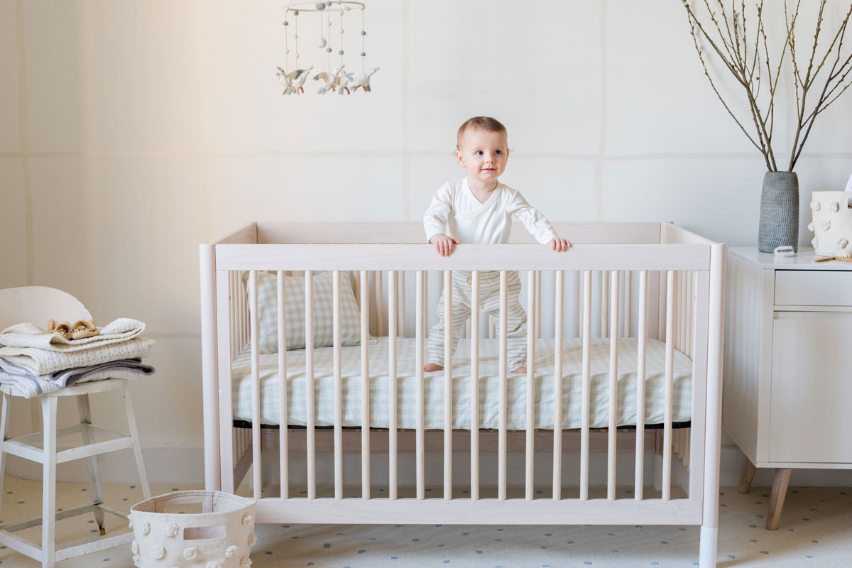 baby boy standing on mattress with pehr checkmate fog crib sheet