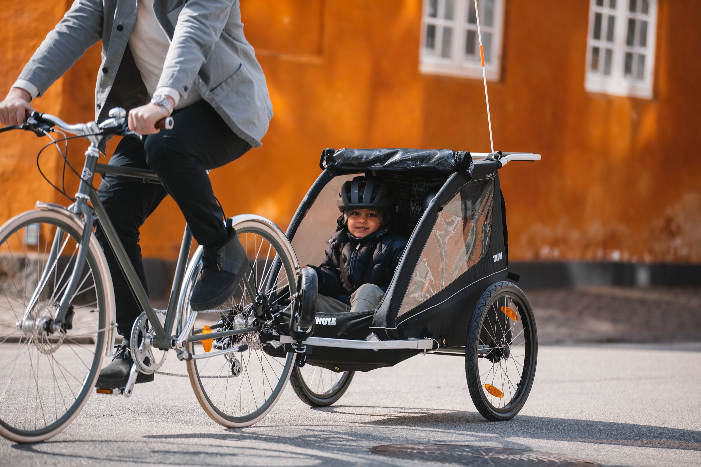 Child sitting in Thule bike trailer coaster XT attached to father bicycle cycling