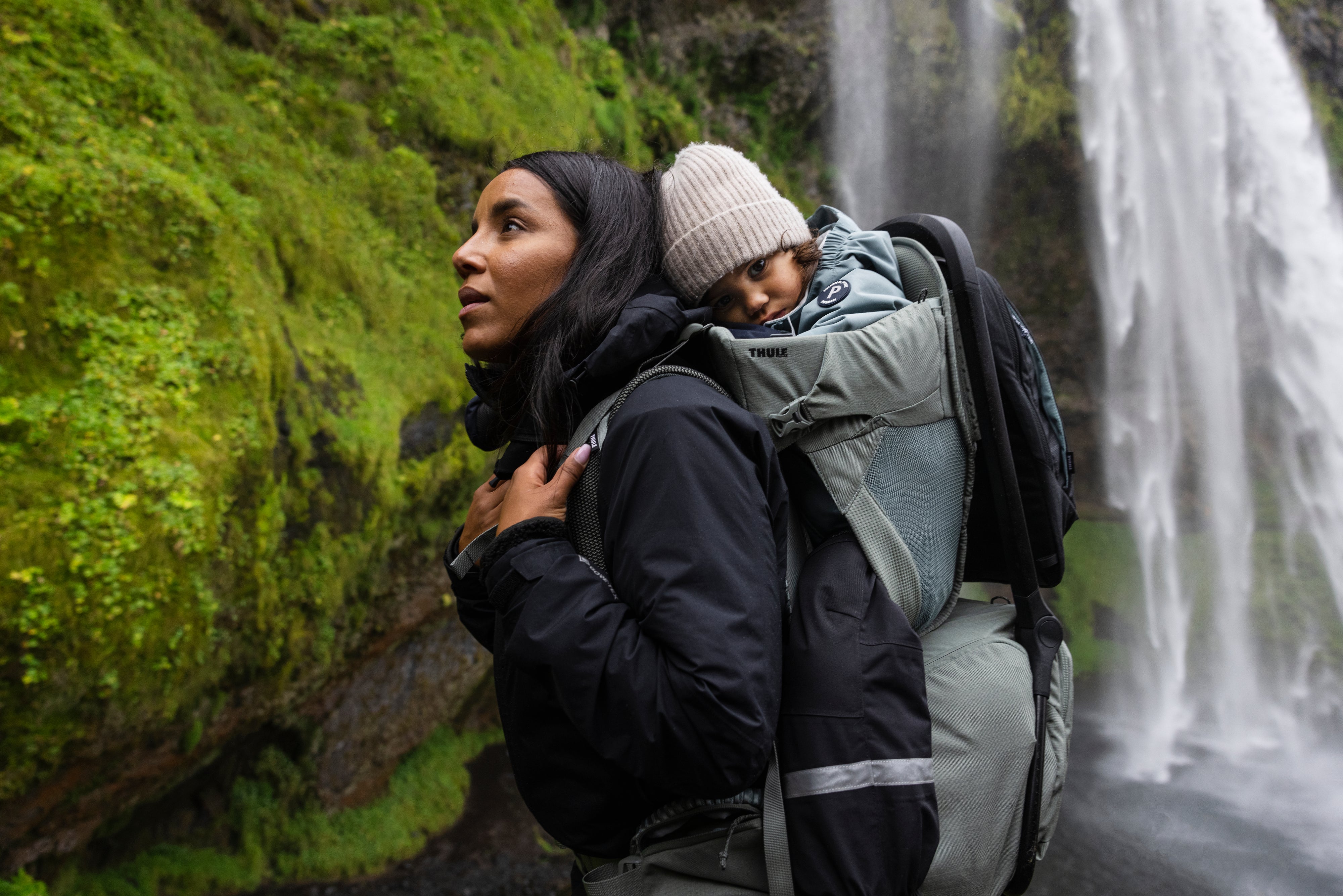Mum carrying child in child carrier backpack while hiking in nature waterfalls