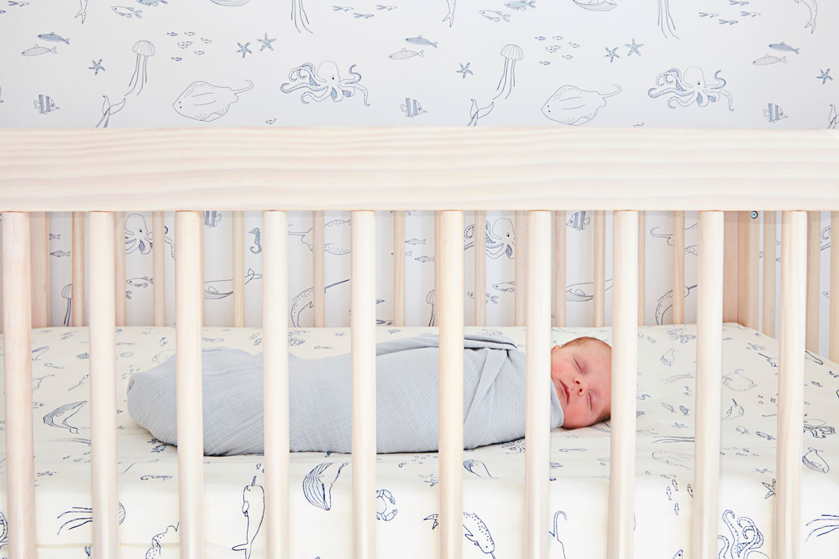 baby sleeping in crib with pehr life aquatic crib sheet