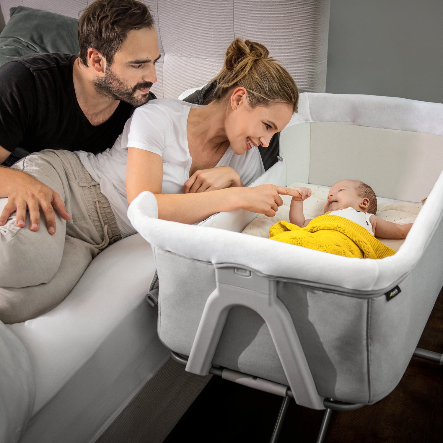 parents on bed with baby in hauck face to me bedside cot